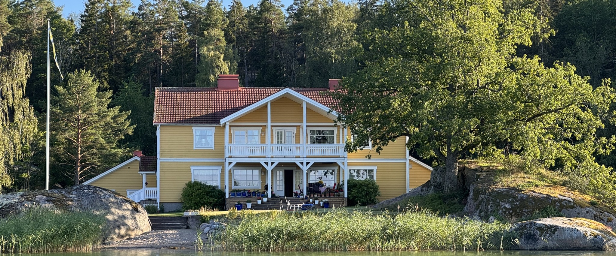 Dalviksnäs gula hus vid vattnet, omgivet av träd och klippor